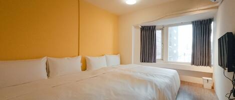 A hotel room with a large bed, a window with curtains, and a mounted television.