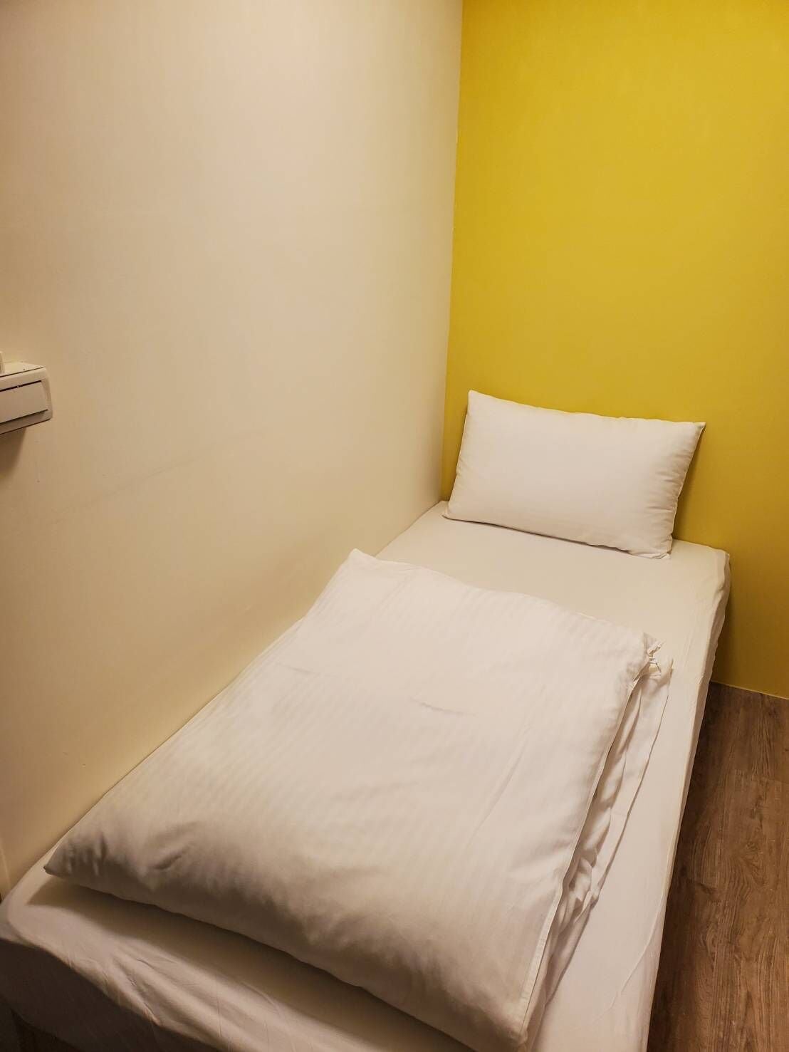 A small, neatly made bed with white linens in a room with yellow and white walls.