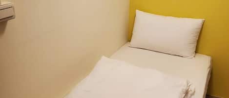 A small, neatly made bed with white linens in a room with yellow and white walls.