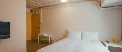 Une chambre d’hôtel avec un lit, une petite table, un téléviseur fixé au mur et une porte donnant sur une autre pièce.