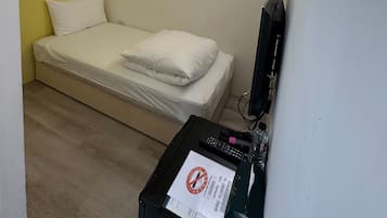 Una habitación pequeña y ordenada con una cama, un escritorio y un televisor montado en la pared.