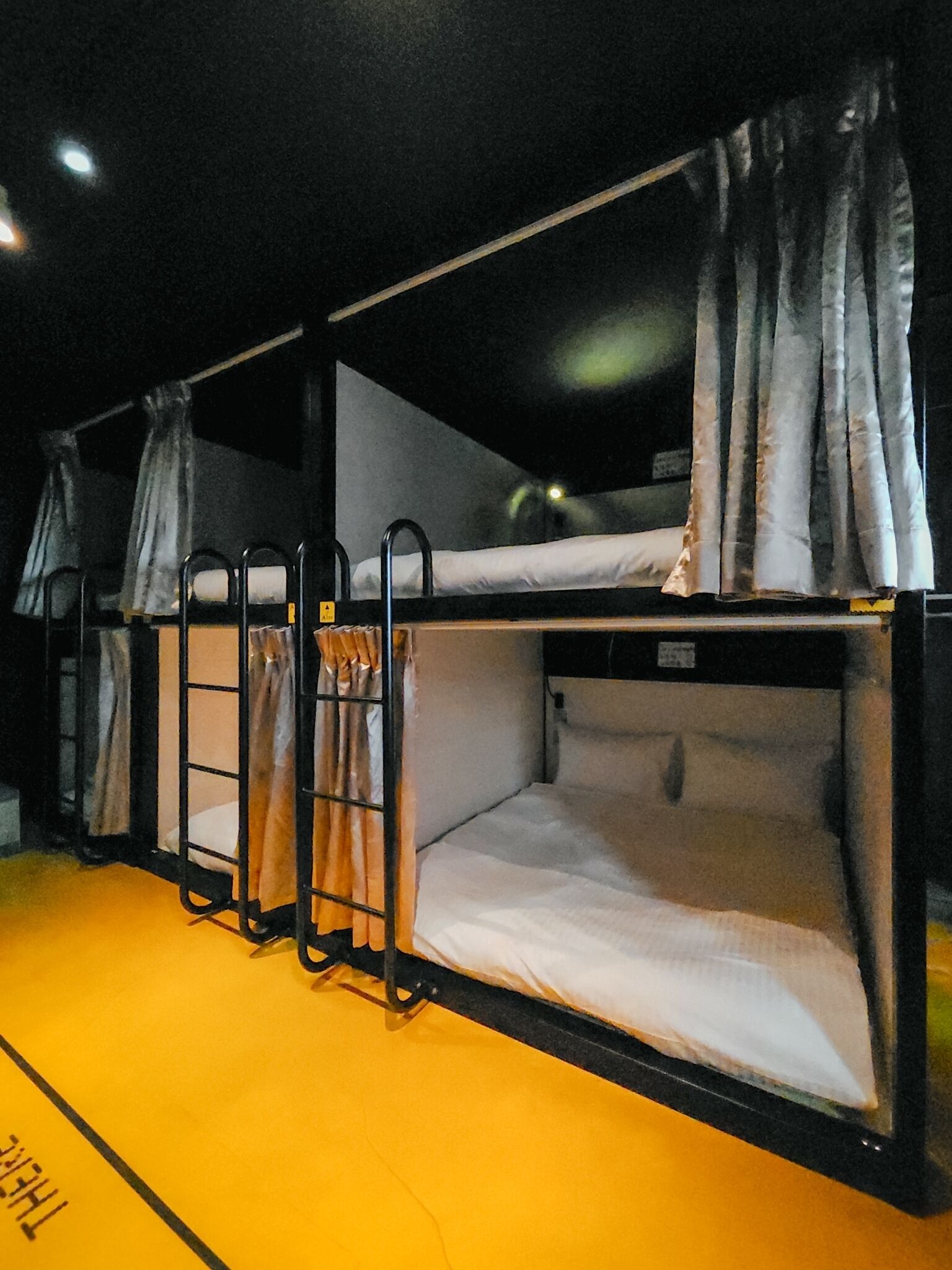 A row of bunk beds with curtains, metal railings, and a yellow floor.