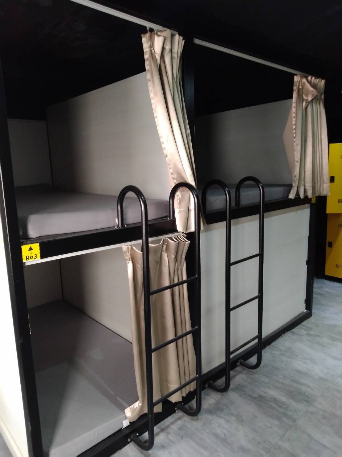 Una cama litera con cortinas, una barra de dominadas y un cartel amarillo.