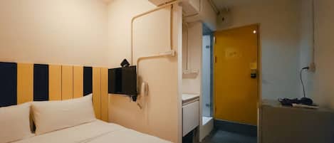 A hotel room with a bed, a desk, a telephone, and a door leading to a bathroom.