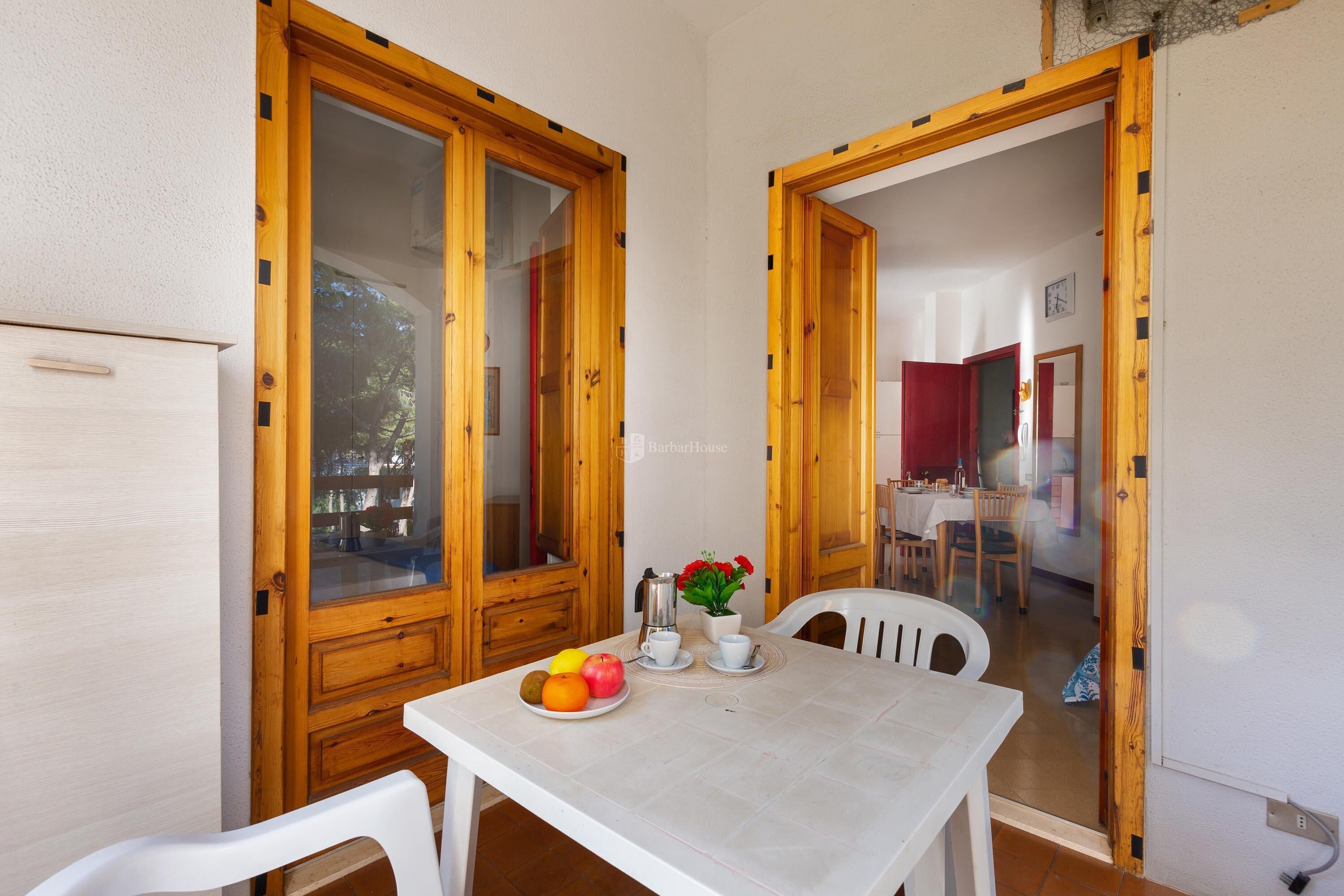 A dining area with a table set for two, a fruit plate, a coffee pot, and a potted plant.