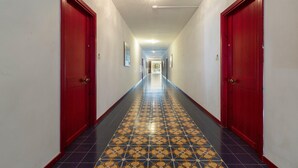 En hall med mönstrade golvplattor, röda dörrar och en lampa i taket.