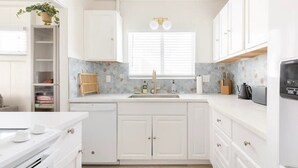 A modern kitchen with white cabinetry, a built-in stove, a sink, and a window with blinds.