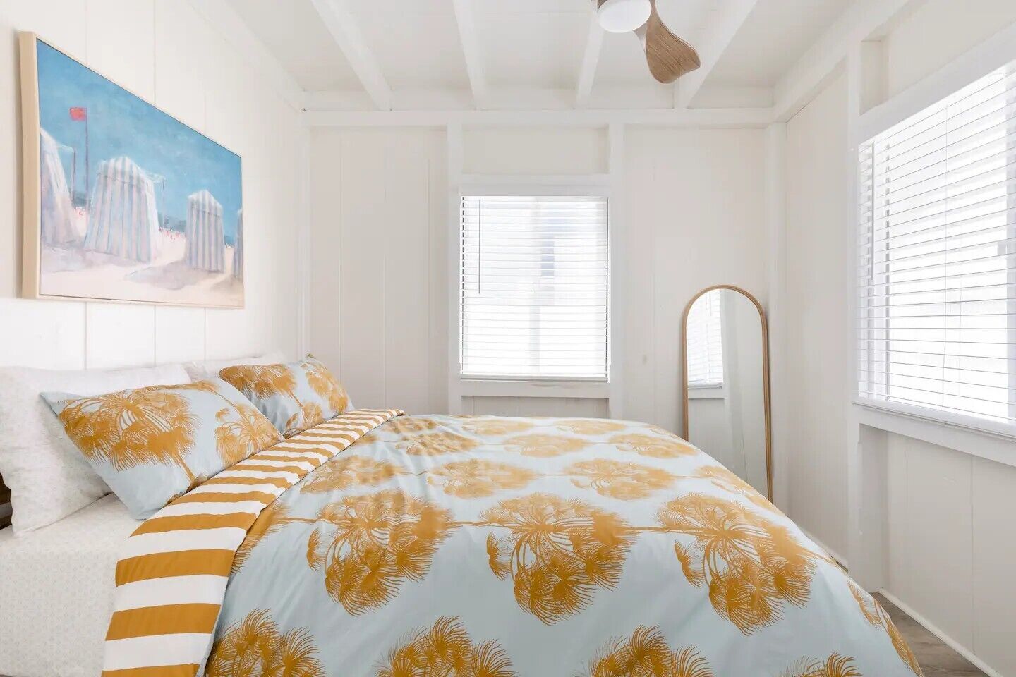 A bedroom with a bed, a painting, a window with blinds, and a ceiling fan.