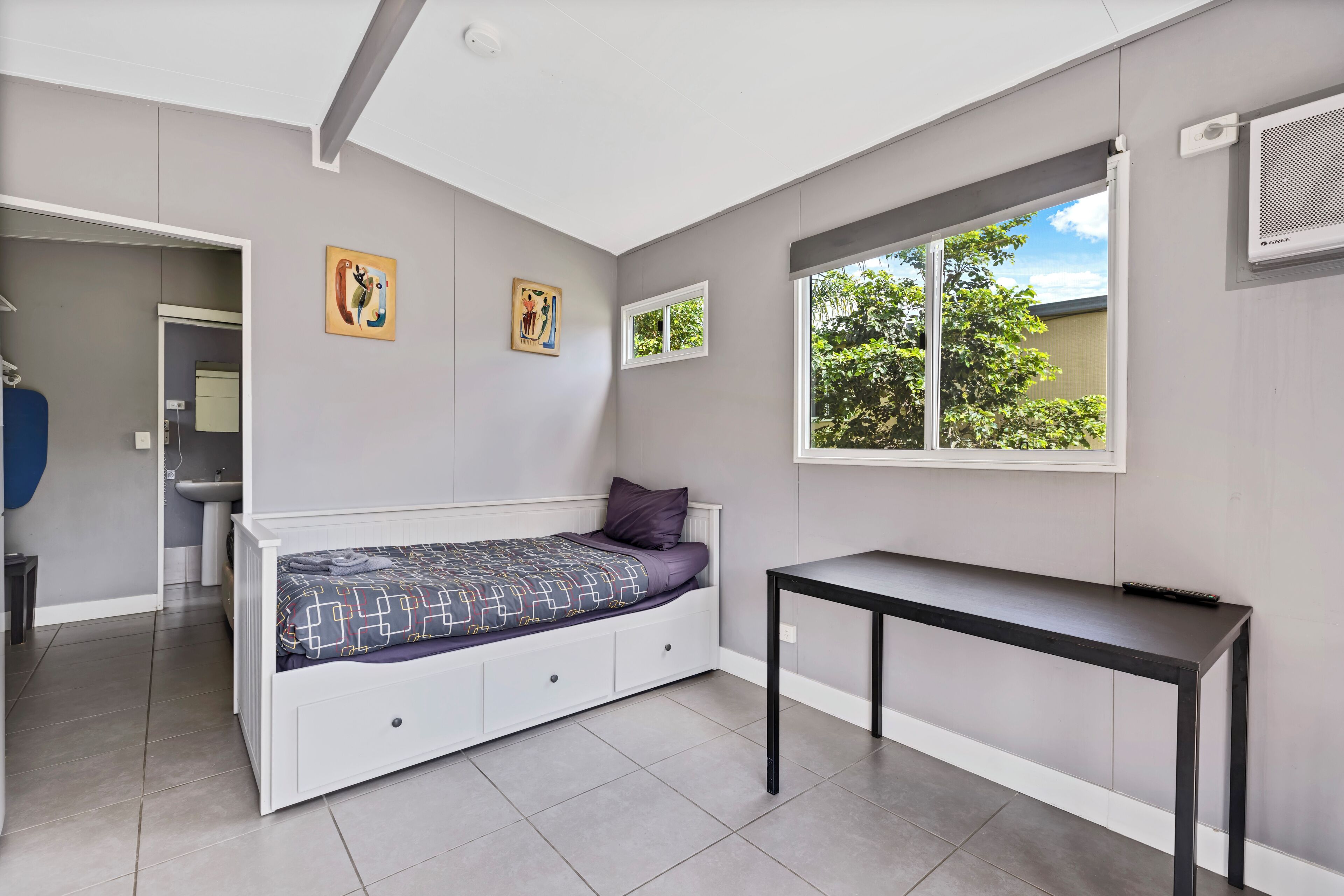 A bedroom with a bed, a window, a table, and artwork on the wall.
