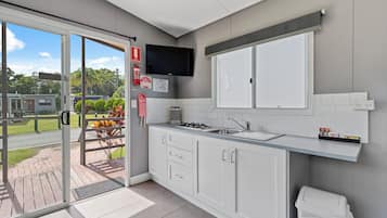 Una cocina moderna con un ventanal grande, armarios blancos, una estufa integrada y un televisor de pantalla plana.