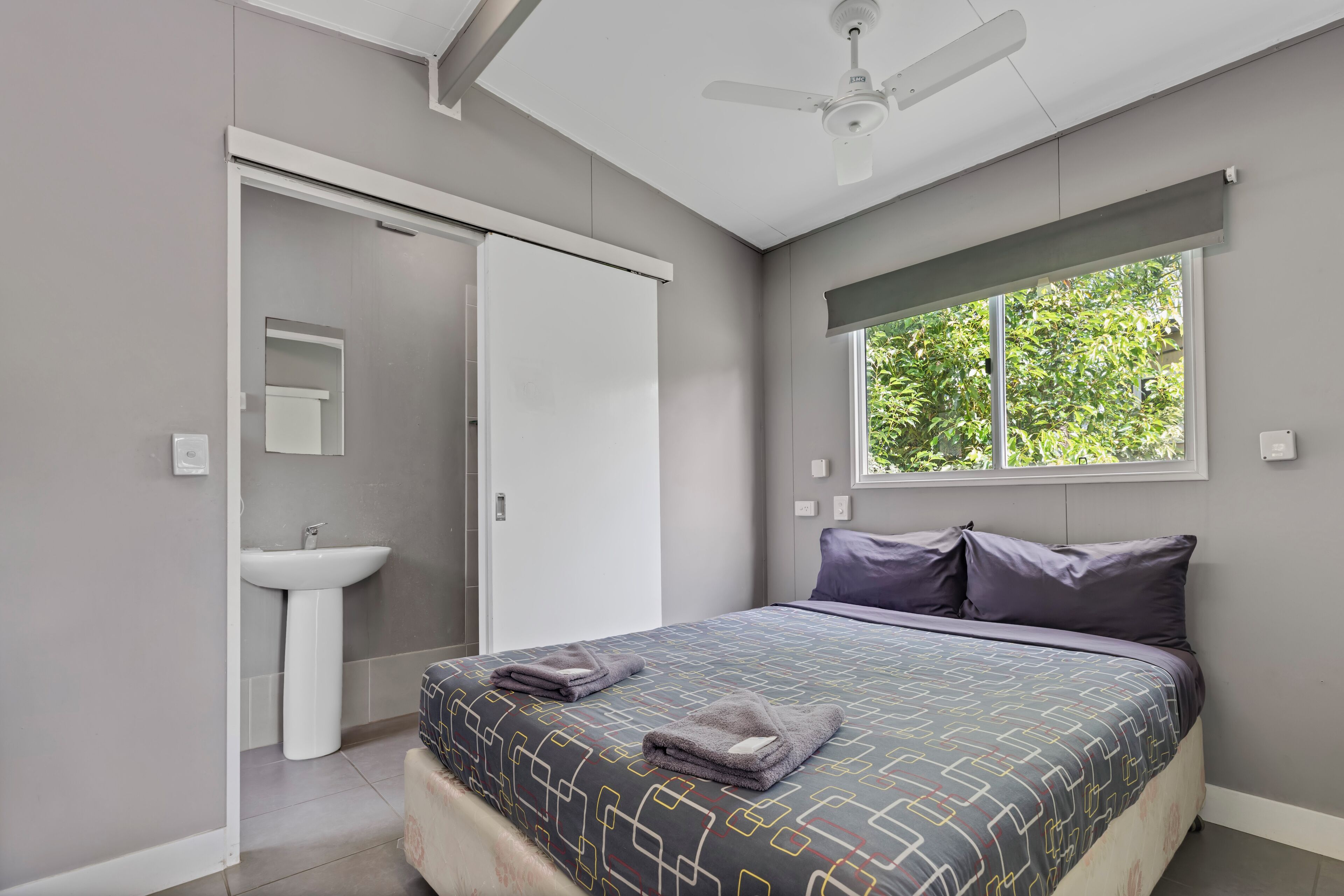 A bedroom with a bed, a window, a ceiling fan, and a bathroom with a sink.