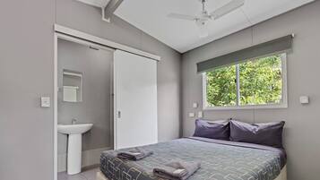 Un dormitorio con cama, ventana, ventilador de techo y baño con lavamanos.
