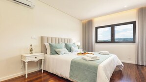 A bedroom with a large bed, a nightstand, a window with a view, and an air conditioning unit. - 6-bed House - Sleeps 12 - Pool, Bbq, Pool Table (Guimarães)