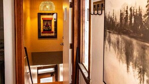 Un couloir au sol en bois, un coin repas avec une table et des chaises, et un grand tableau encadré accroché au mur.
