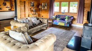 Acogedor interior de una cabaña de madera con un sofá de cuero, un banco colorido acolchado y una chimenea.