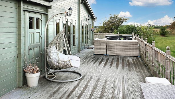 Una terraza de madera con una silla colgante, un banco acolchado y una planta en maceta.