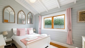 Un dormitorio con cama, mesitas de noche, una ventana con cortinas y un espejo en la pared.