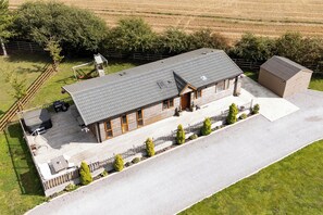 Une maison à deux étages avec un toit en pente, une terrasse couverte et une cour clôturée.