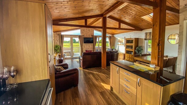Une cuisine spacieuse avec des meubles en bois et un grand îlot central, un coin salon confortable avec un canapé et des fauteuils, et une vue sur l’extérieur grâce à une porte-fenêtre coulissante.
