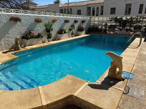 Une piscine bordée de pierres, une statue en pierre et des plantes en pot fixées au mur.
