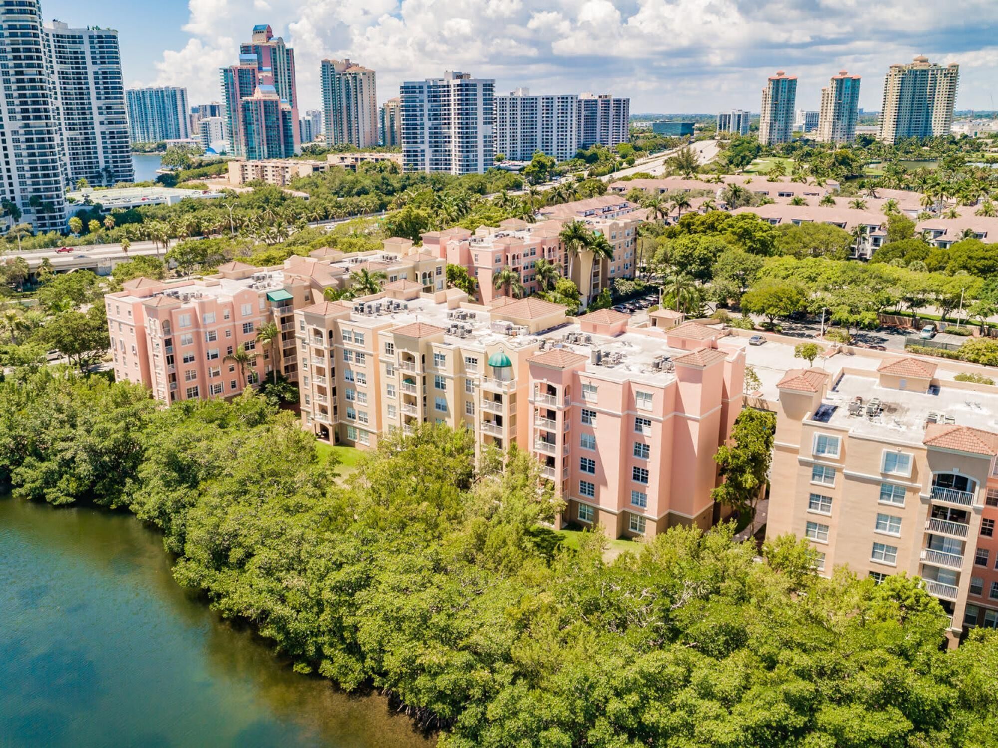 A high-rise residential building with multiple floors, surrounded by lush greenery and a body of water.