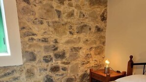 A room with a stone wall, a bed with a textured mattress, and a bedside table with a lamp.