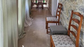 A corridor with a stone wall, wooden ceiling, and a dining area with chairs and a table.