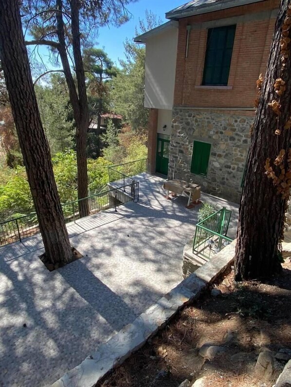 A stone building with a green door, a balcony with a metal railing, and surrounding trees.