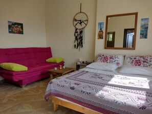 Une chambre avec un lit, un canapé rose, une petite table en bois et un attrape-rêves accroché au mur.