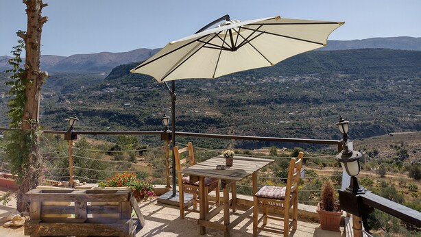 A wooden table and chairs on a balcony with a view of a mountainous landscape.