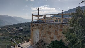 A stone building with a balcony, a stone wall, and a view of a hilly landscape.