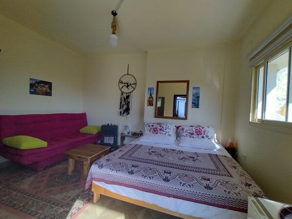 Une chambre avec un lit, un canapé rose, une petite table et un attrape-rêves accroché au mur.