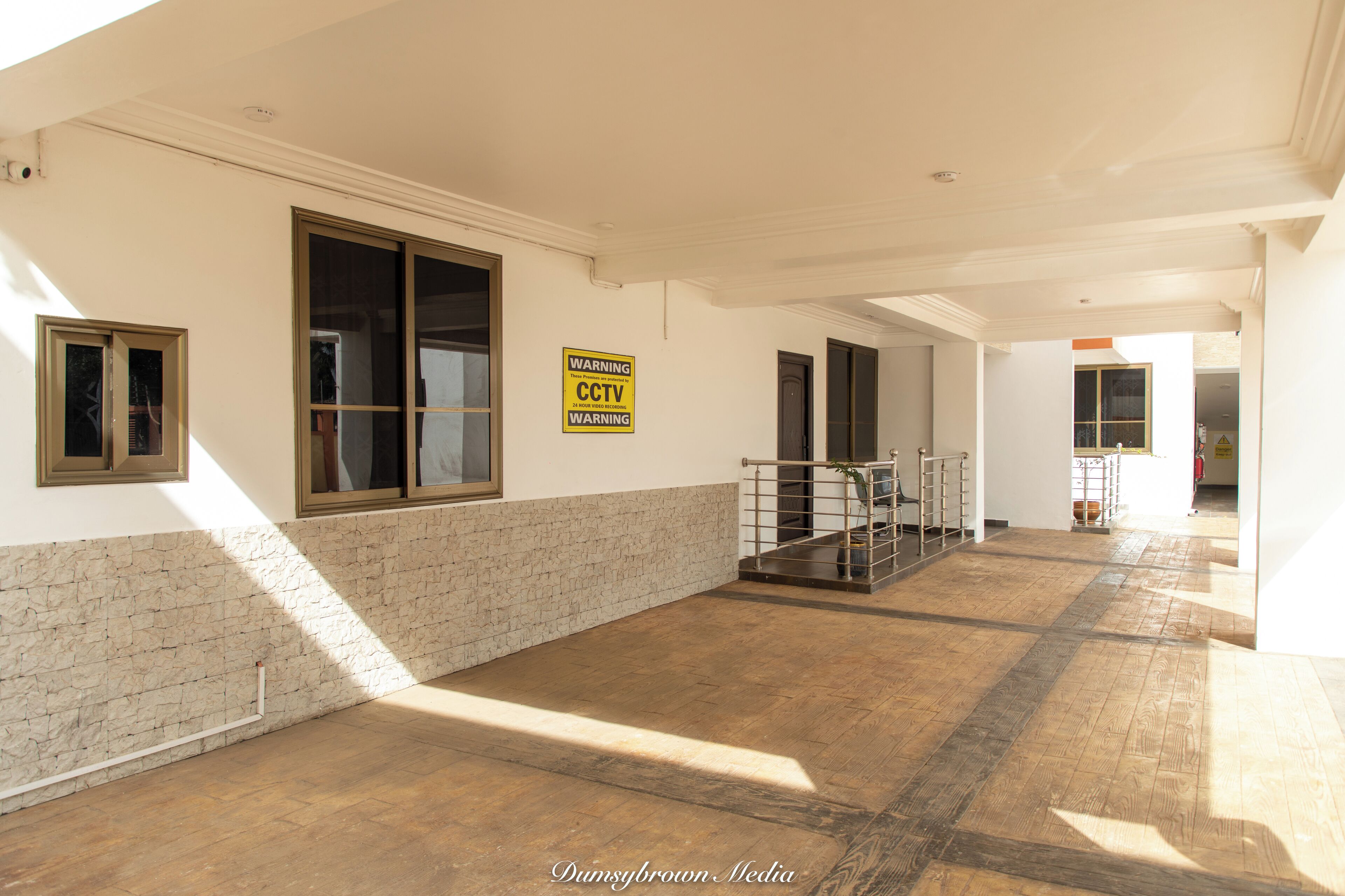 A spacious corridor with stone walls, large windows, and a CCTV warning sign.