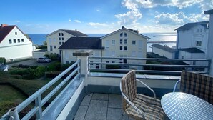 A balcony with a view of the sea, a white building, and a checkered chair.
