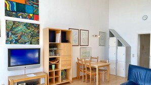 A modern living room with a flat-screen TV, wooden entertainment unit, dining table with chairs, and a blue sofa.