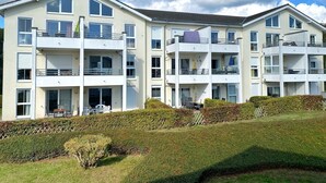 A multi-story residential building with balconies, a flat roof, and a well-maintained lawn.