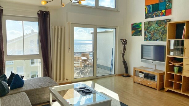 A spacious living area with a sofa, a glass coffee table, a TV, and artwork on the walls.