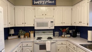 A kitchen with white cabinets, a microwave, stove, and a sign that says "this is our happy place." - Welcoming, Roomy and Conveniently Located! (Hot Springs Village)