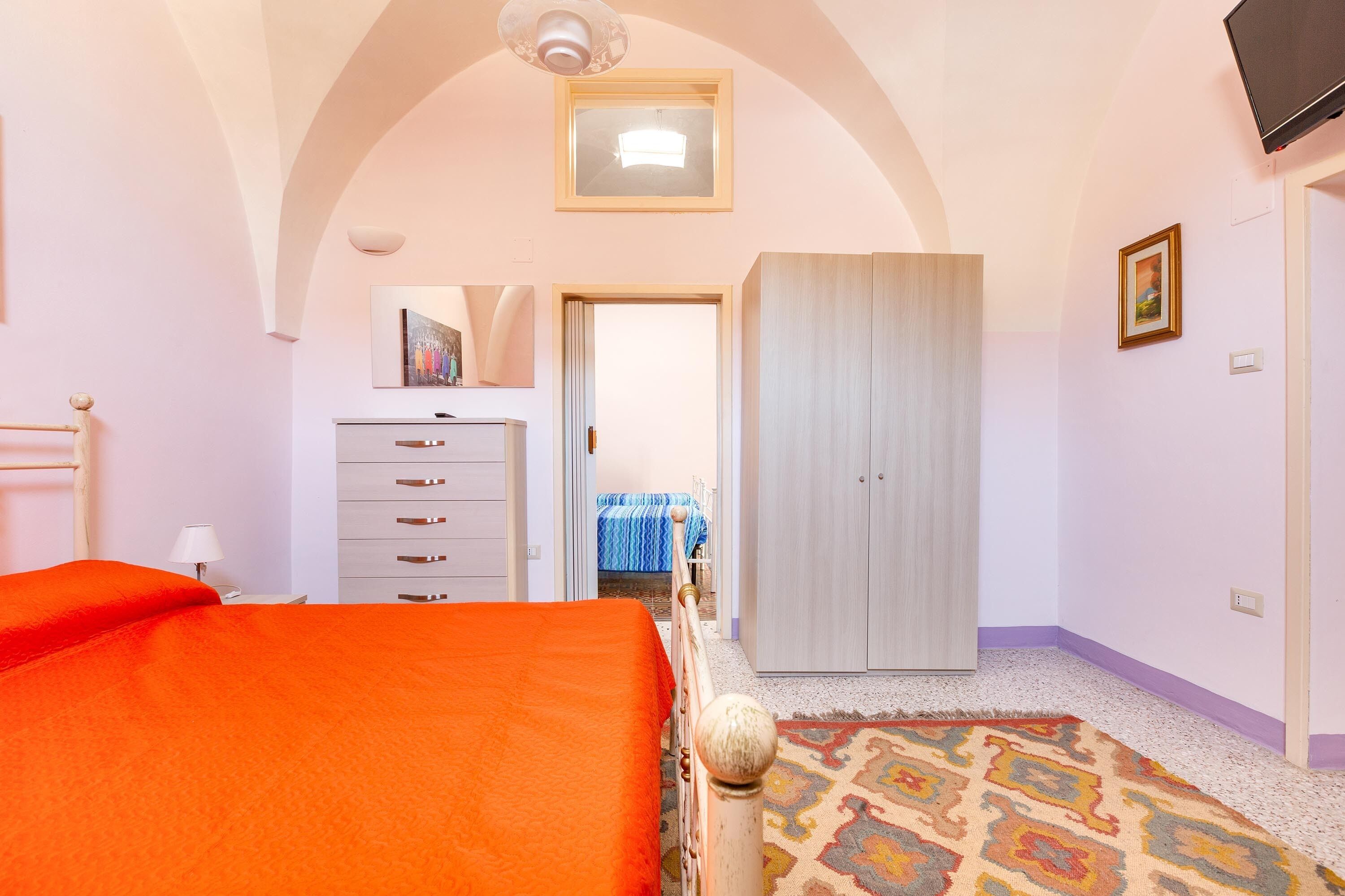 A bedroom with a bed, a wardrobe, a dresser, and a door leading to another room.