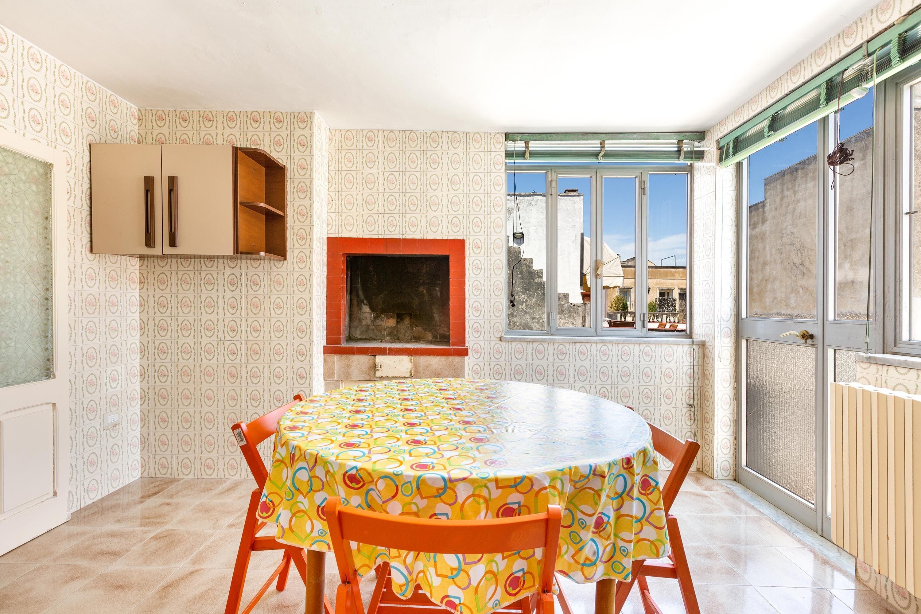 A dining area with a round table, orange chairs, and a colorful tablecloth.