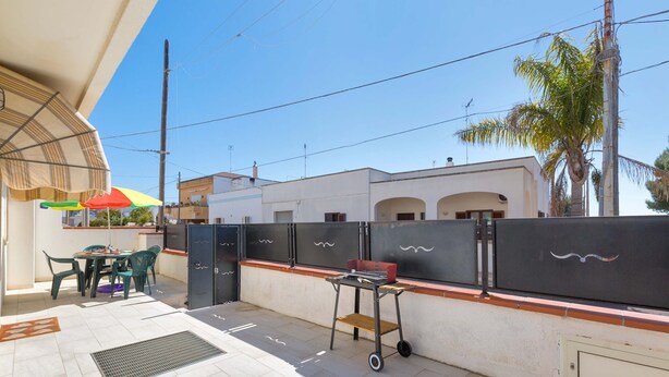 An outdoor patio with a table and chairs, a grill cart, and a palm tree. - 2808 Case al Tacco - Appartamento Terra by Barbarhouse (Castrignano del Capo)