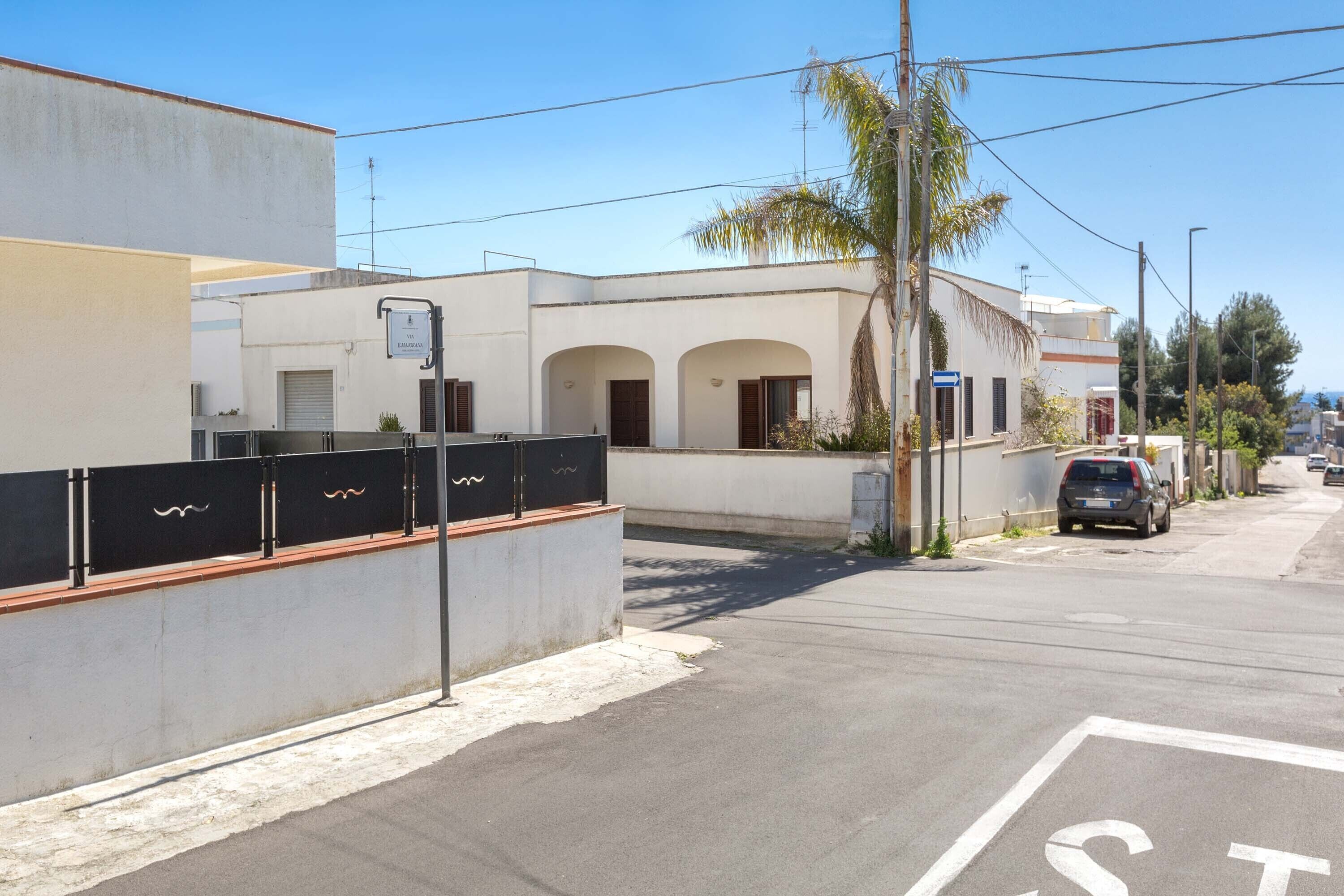 A street view with a building featuring a white facade, arched windows, and a palm tree.