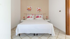 A double bed with a white bedspread, two nightstands with lamps, and floral artwork on the wall. - 2808 Case al Tacco - Appartamento Terra by Barbarhouse (Castrignano del Capo)