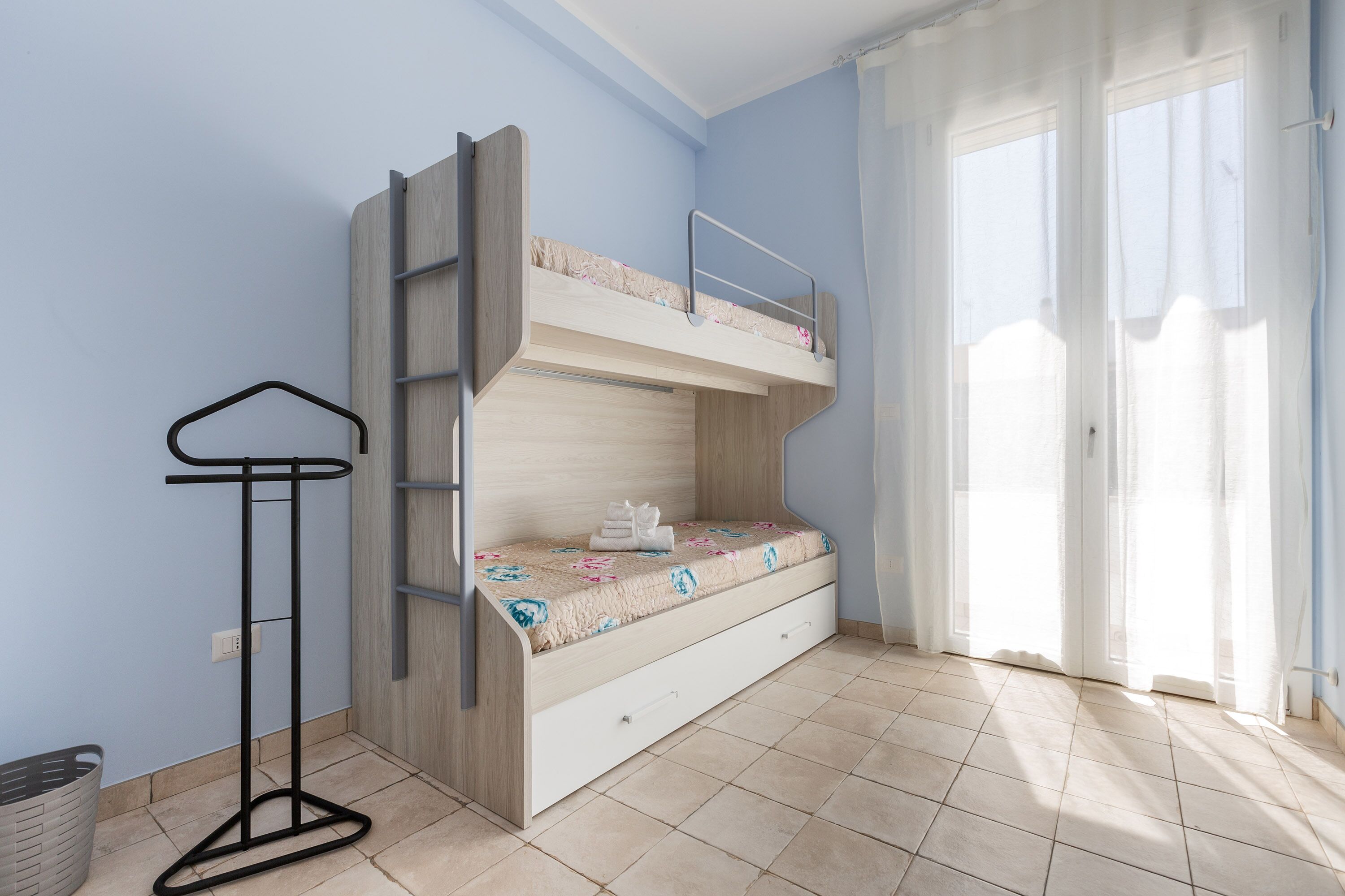 A bunk bed with a ladder, a small table, and a basket against a wall.