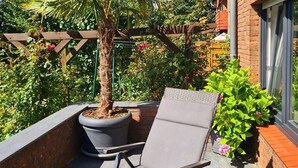 A patio with a lounge chair, a potted palm tree, and a brick wall. - Large time-out apartment - modern, close to the beach and with a large garden terrace - (Neustadt in Holstein)
