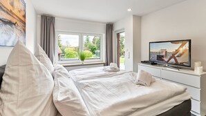 A bedroom with a large bed, a television, and a window with a view of greenery. - Large time-out apartment - modern, close to the beach and with a large garden terrace - (Neustadt in Holstein)