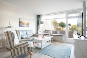 A modern living room with a striped sofa, a white coffee table, and a large window with a view of the outdoors.