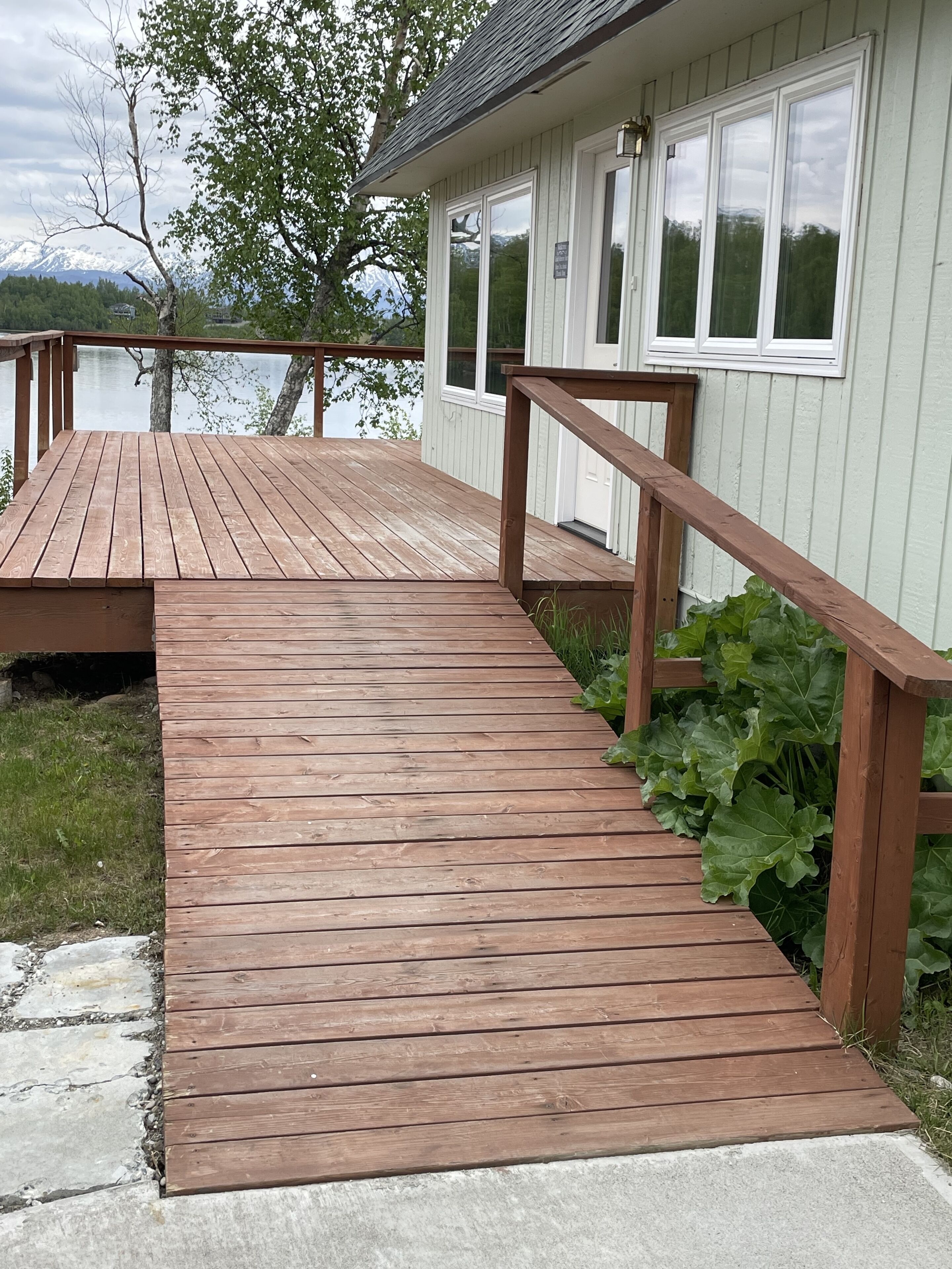 Eine Holzterrasse führt zu einem Haus mit Blick auf einen See und Berge.