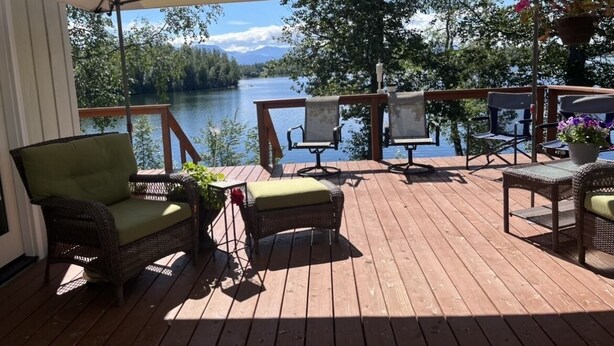 Een houten terras met rieten meubilair en uitzicht op een meer.