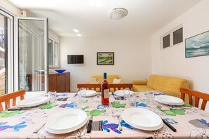 Uma área de refeições com uma mesa posta para quatro pessoas, uma garrafa de vinho tinto e um sofá ao fundo.